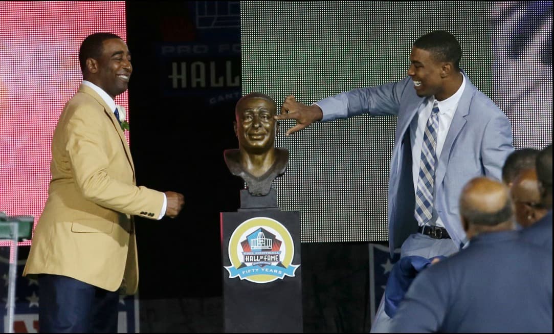 El receptor Cris Carter durante la ceremonia donde fue inducido al Salón de la Fama. Su hijo Duron toca el rostro esculpido del homenajeado.