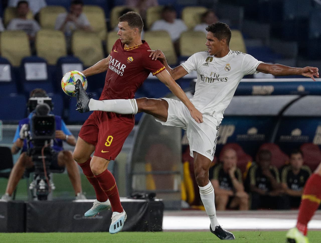 Raphael Varane le mete la pierna a Edin Dzeko para robarle el balón.