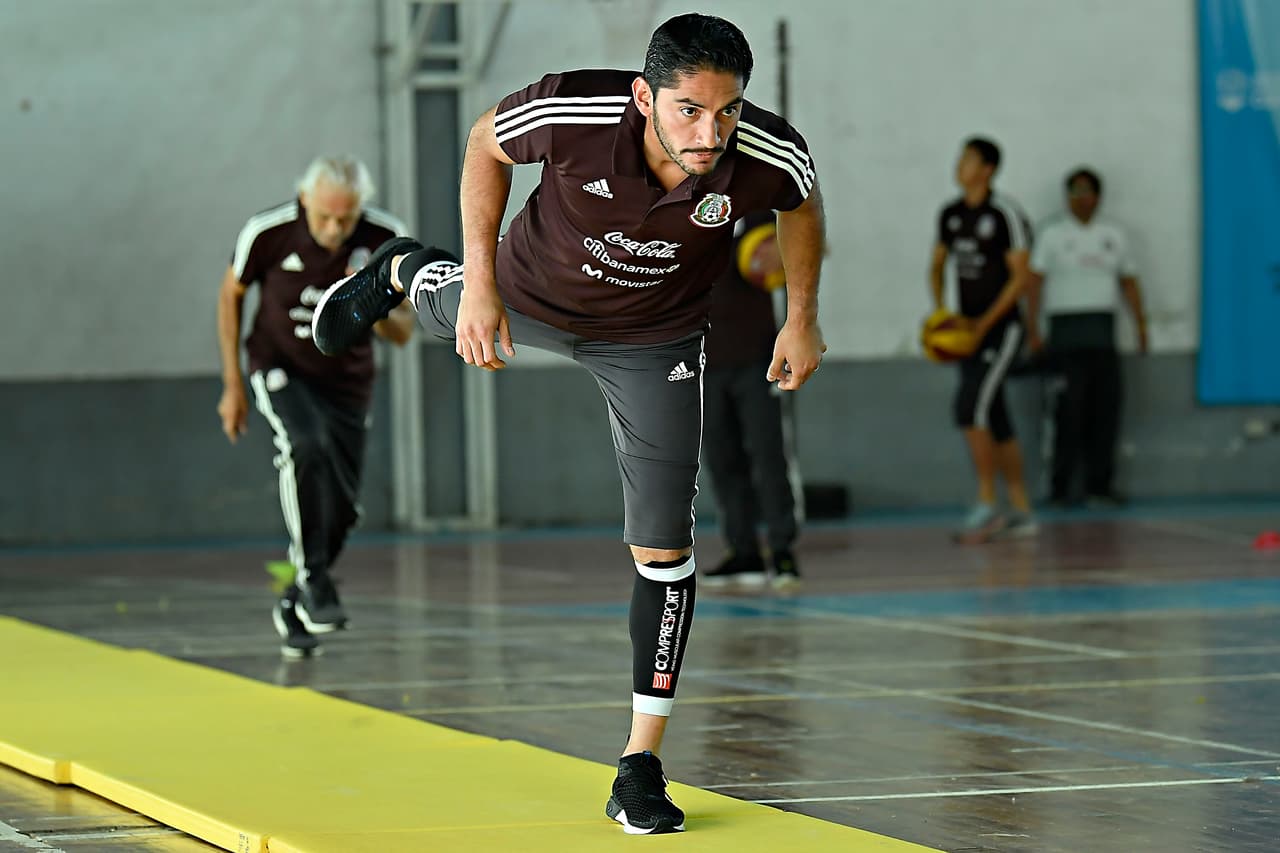 Aquí se aprecia a José de Jesús Corona hacer estiramientos y de fondo se ve a un integrante de la selección a punto de hacer un tiro a un aro dentro de este gimnasio donde pudieron tener actividad.