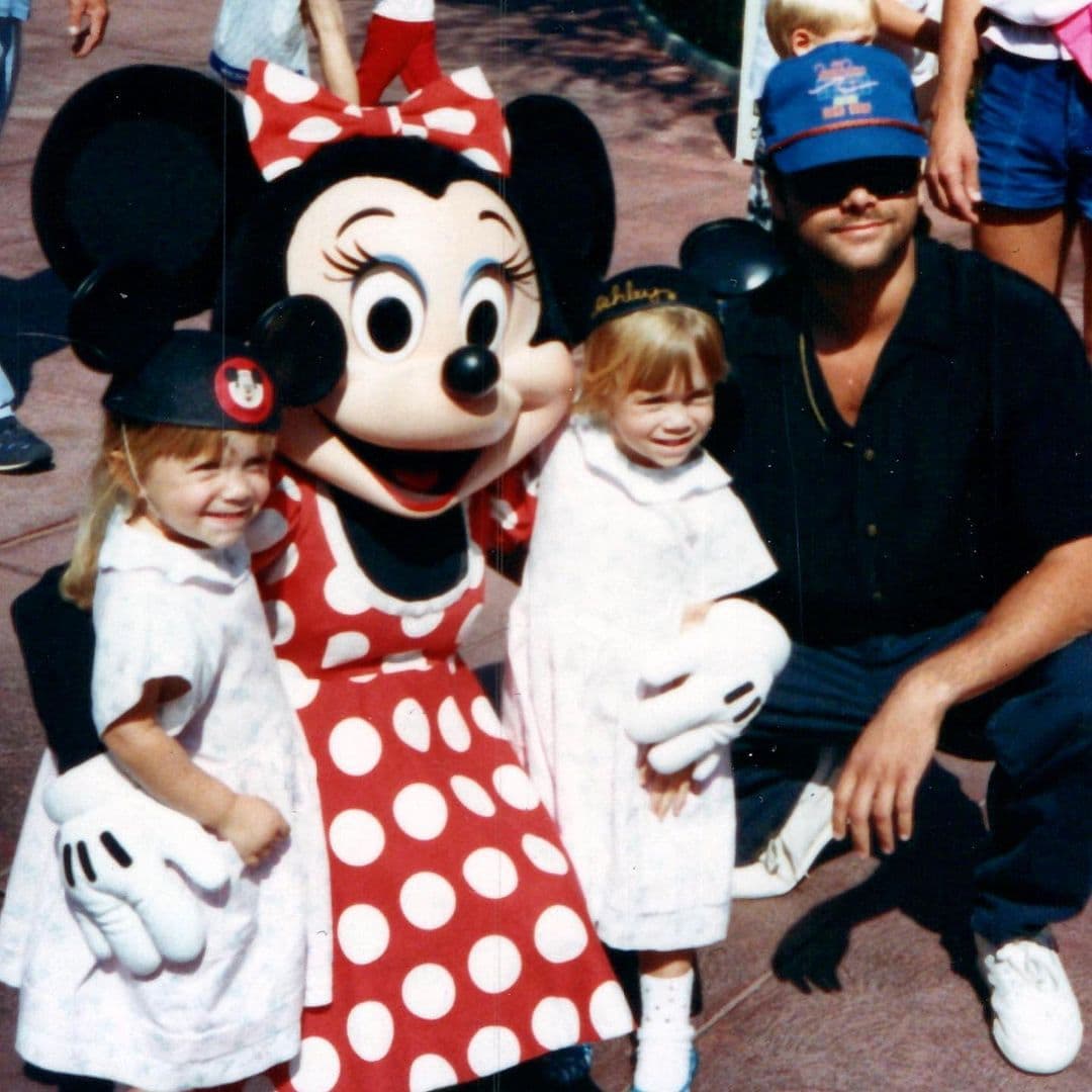 Se puede ver a una joven Mary-Kate y Ashley Olsen posando con Minnie Mouse mientras usan sombreros con orejas de ratón, mientras Stamos se agacha a su lado.