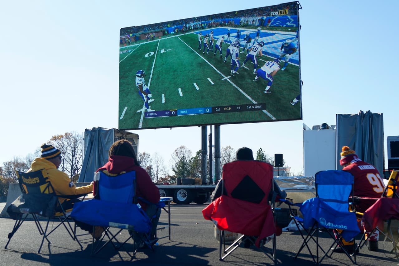Football fans watch the Detroit Lions and Minnesota Vikings play on a big screen television in the FedEx Field parking lot before an NFL football between the Washington Redskins and the New York Giants in Landover, Md., Thursday, Nov. 23, 2017. (AP Photo/Mark Tenally)