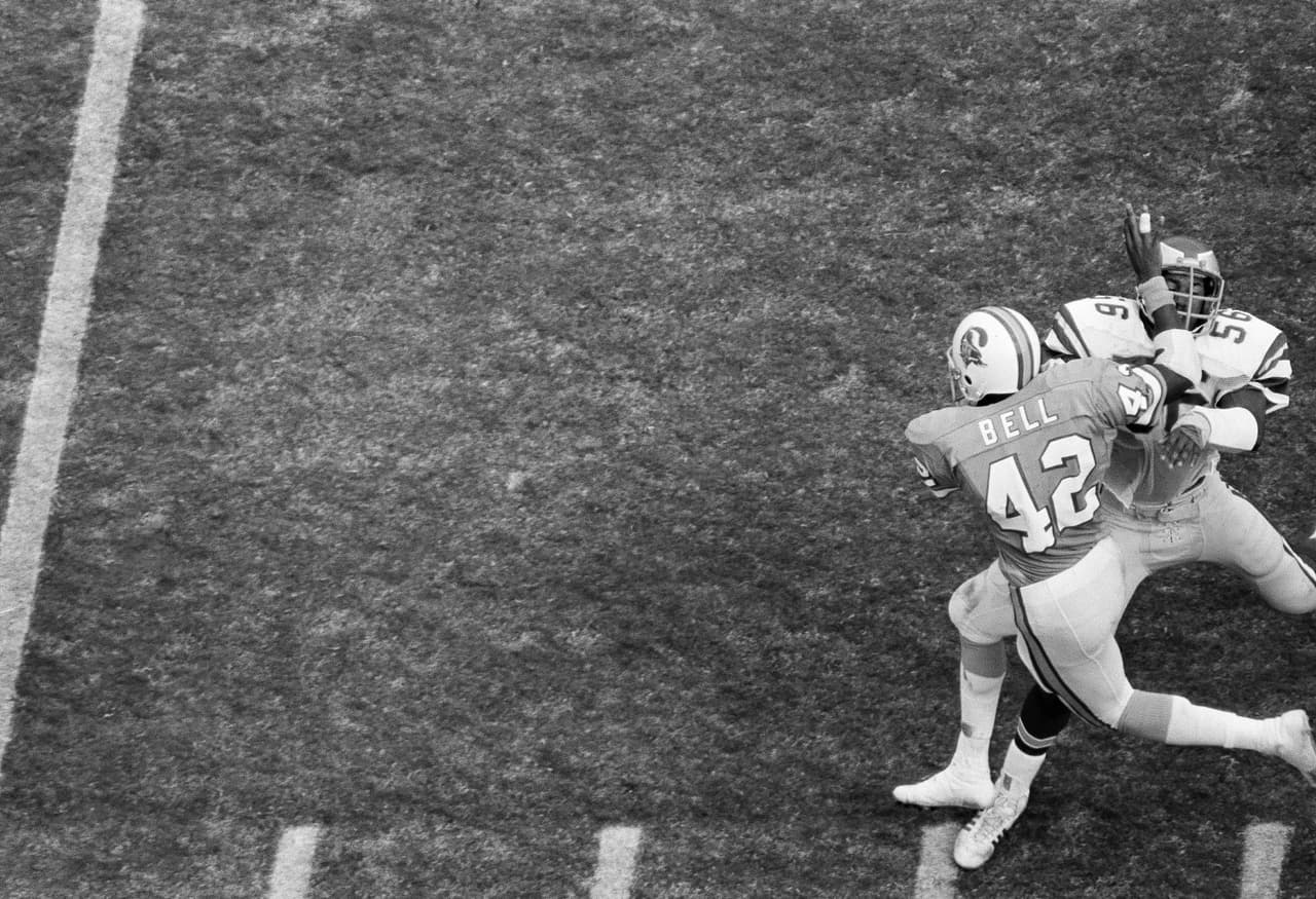 1977 RICKY BELL | RB USC - 
<b>Tampa Bay Buccaneers</b>
<br>
<br>Ricky Bell fue el pick #1 de Tampa Bay Buccaneers en 1977. En la imagen empuja al linebacker Jerry Robinson de Philadelphia Eagles en los Playoffs de la NFC. Bell rompió un récord de la NFL por intentos de carrera en la postemporada con 38 acarreos. Los Bucs derrotaron a los Eagles 24-17 en Tampa, Florida, el 30 de diciembre de 1979.