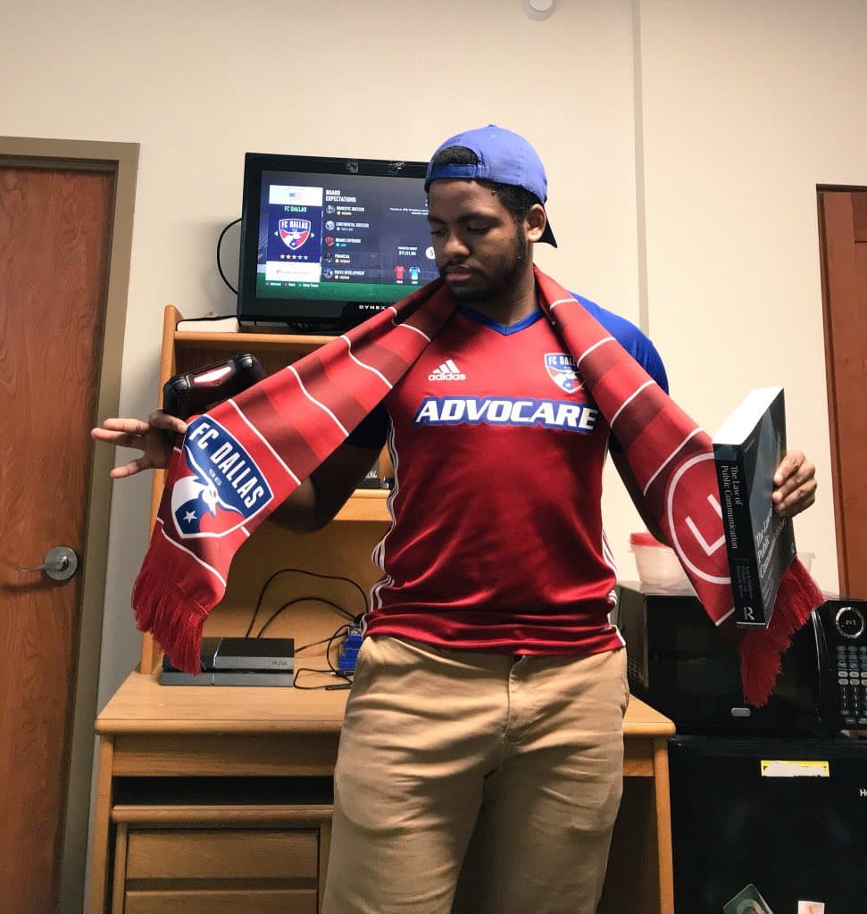 El aficionado del FC Dallas se debate entre estudiar para el examen o llevar a su querido FC Dallas a la gloria en un popular videojuego, mientras porta la nueva playera de los Hoops.