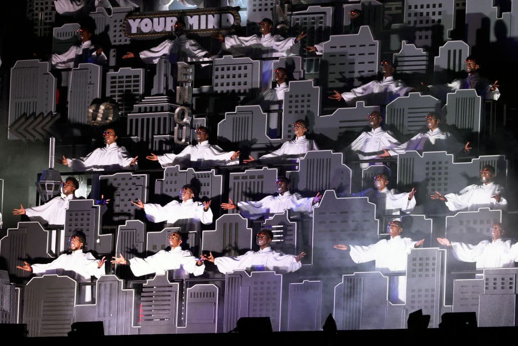 Detrás de él había una banda y un coro intercalados entre una ciudad neón, y a menudo estaba rodeado de bailarines, con la cara vendada, como en sus videos musicales.