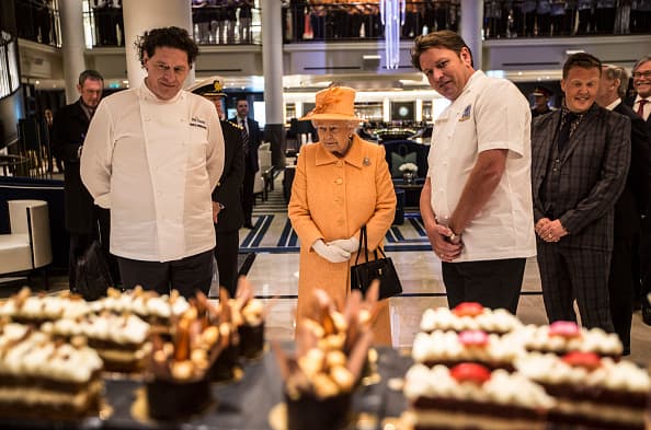 LONDON, ENGLAND - MARCH 10: Queen Elizabeth II looks at cakes and sweets on the patisserie counter on board the new P&O cruise liner 'Britannia' with chefs Marco Pierre White (left) and James Martin (Right) during a tour of the ship at the official naming ceremony of 'Britannia' the new flagship P&O fleet at Ocean Cruise Terminal on March 10, 2015 in Southampton, England. Britannia will carry over 3647 passengers and at 141,000 tons she will boost P&O's cruise ship capacity by 24%. (Photo by Richard Pohle - WPA Pool /Getty Images)