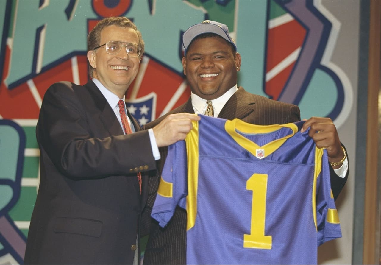 1997 ORLANDO PACE | T Ohio State - 
<b>St. Louis Rams</b>
<br>
<br>El liniero ofensivo Orlando Pace sostiene su nuevo jersey de los St. Louis Rams, proveniente de los Ohio State Buckeyes, junto al comisionado Paul Tagliabue como la primera selección general en el draft el jueves17 de abril de 1997.