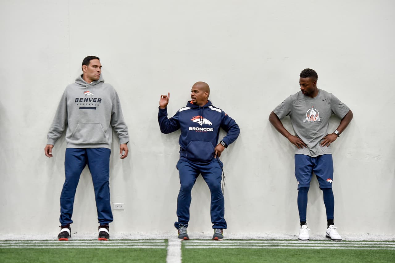 Sánchez y Emmanuel Sanders escuchando las intrucciones para estiramiento y acodicionamiento del coach Dennis Love.