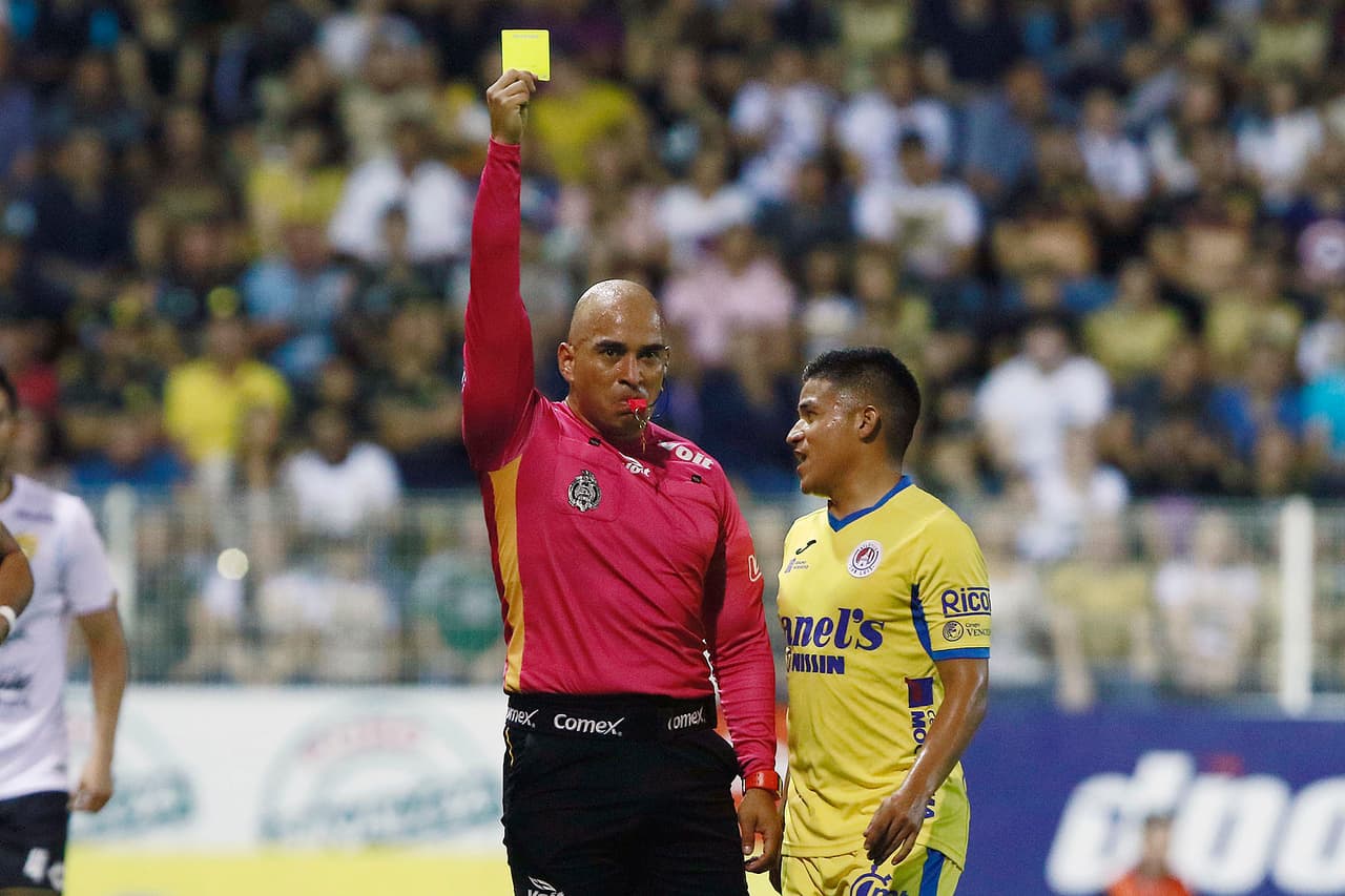 Juan Andrés Esquivel, arbitro central de este partido, muestra tarjeta de amonestación a un jugador de los potosinos, cuando el duelo estaba empezando a calentarse más de la cuenta.