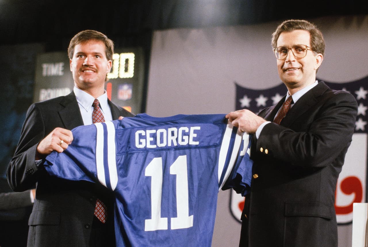 1990 JEFF GEORGE | QB Illinois - 
<b>Indianapolis Colts</b>
<br>
<br>El mariscal de campo Jeff George sostiene su nuevo jersey de los Indianapolis Colts mientras posa para una foto con el comisionado de la NFL Paul Tagliabue en el Draft de la NFL de 1990 el 22 de abril de 1990 en Nueva York.