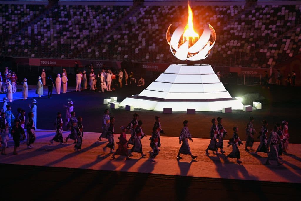 Miembros del equipo artístico recorren parte del terreno, alrededor del pebetero en el que todavía se veía ardiendo la llama olímpica.