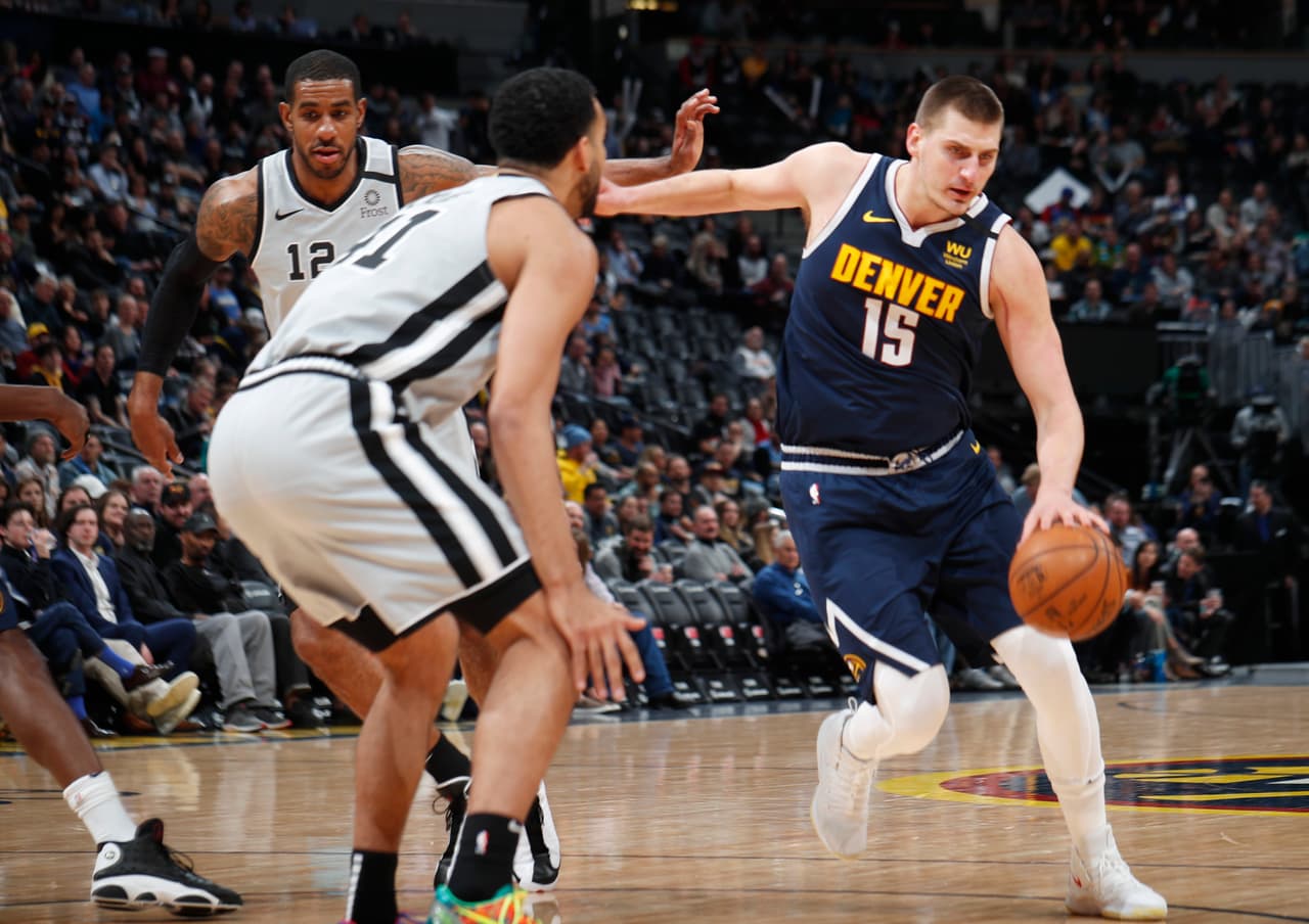 El centro de los Denver Nuggets Nikola Jokic conduce el balón hasta la canasta pese a la marca de Trey Lyles y LaMarcus Aldridge de los San Antonio Spurs.