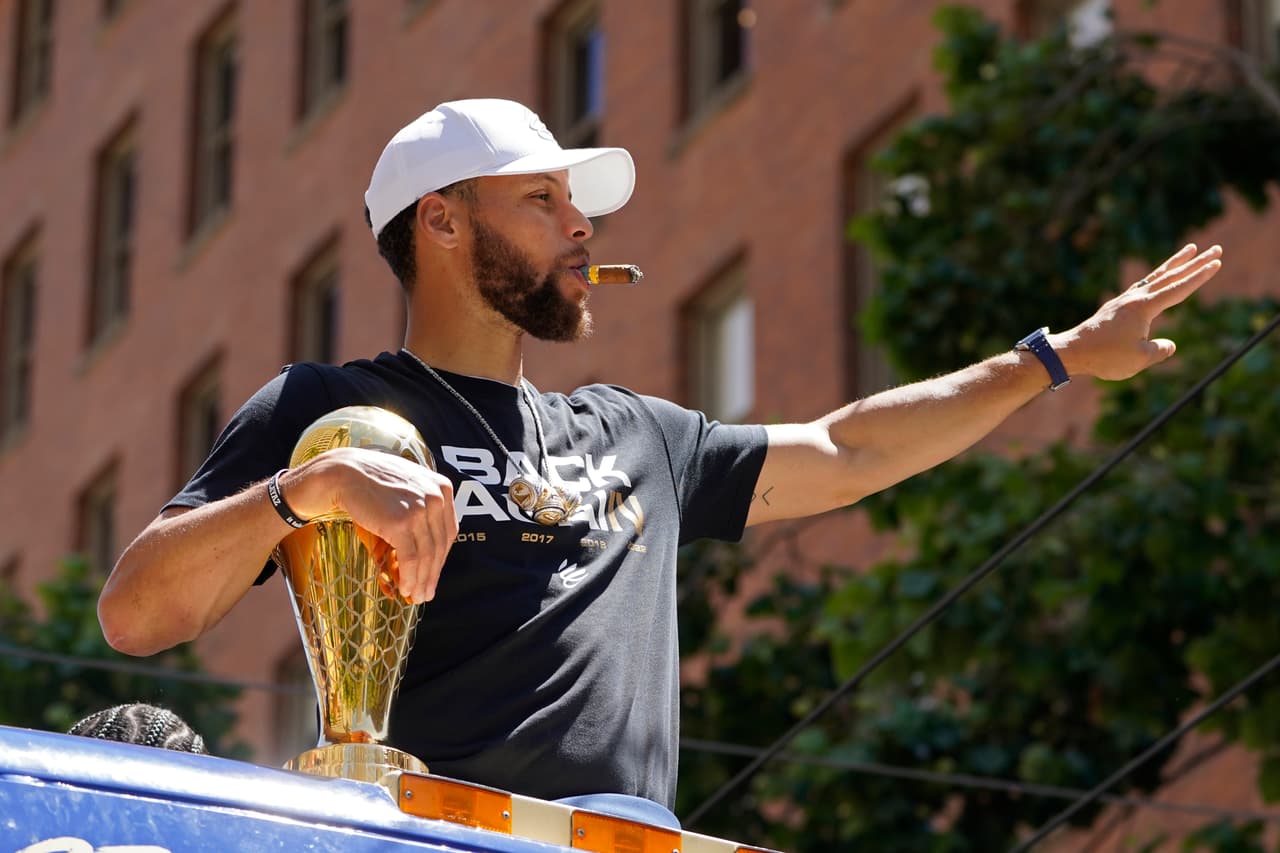 Stephen Curry fuma un cigarro y saluda mientras cabalga en el desfile del campeonato de la NBA de los Golden State Warriors en San Francisco, el lunes 20 de junio de 2022. (Foto AP/Eric Risberg)