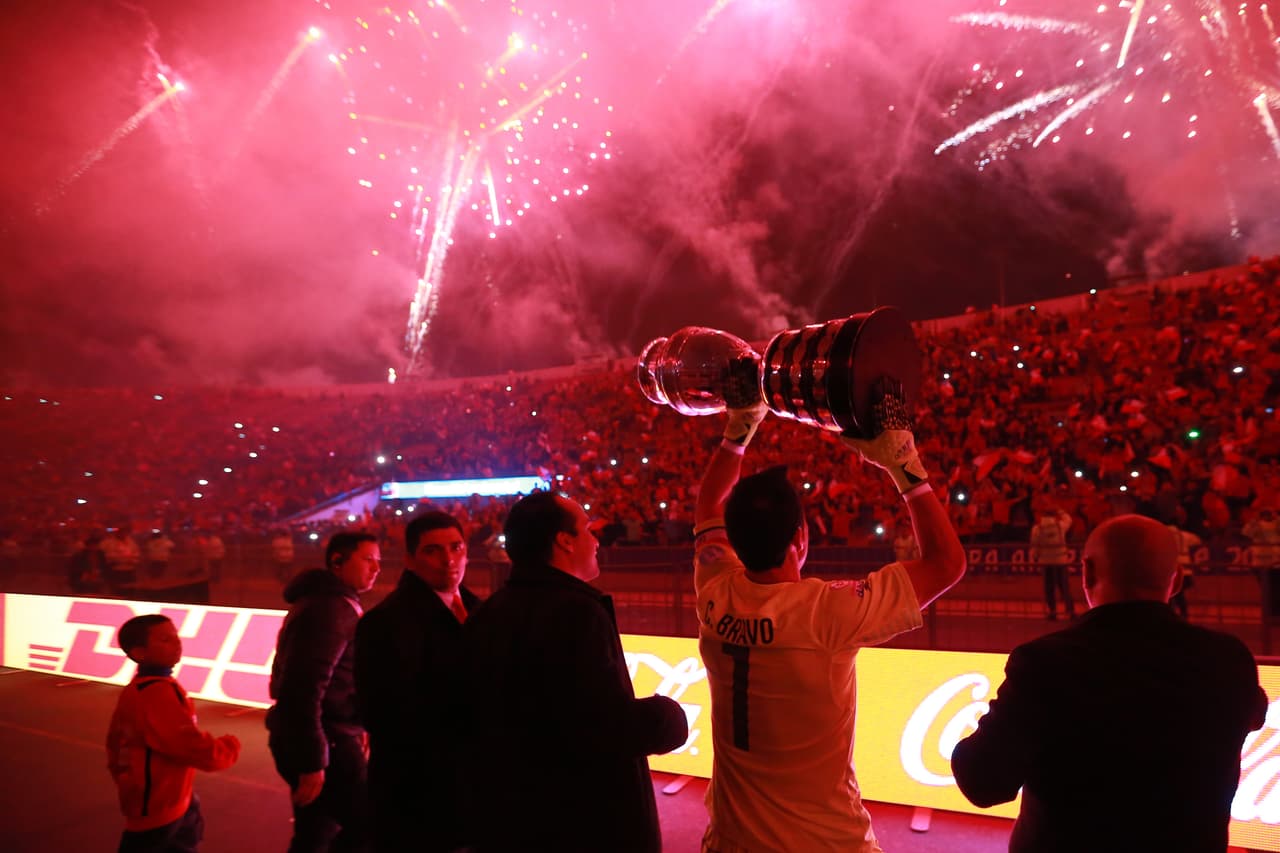 En medio de un cielo lleno de fuegos artificiales, Claudio Bravo carga la copa de campeón y se la muestra a su afición en la final de la Copa América que ganó Chile a su similar de Argentina en penales.