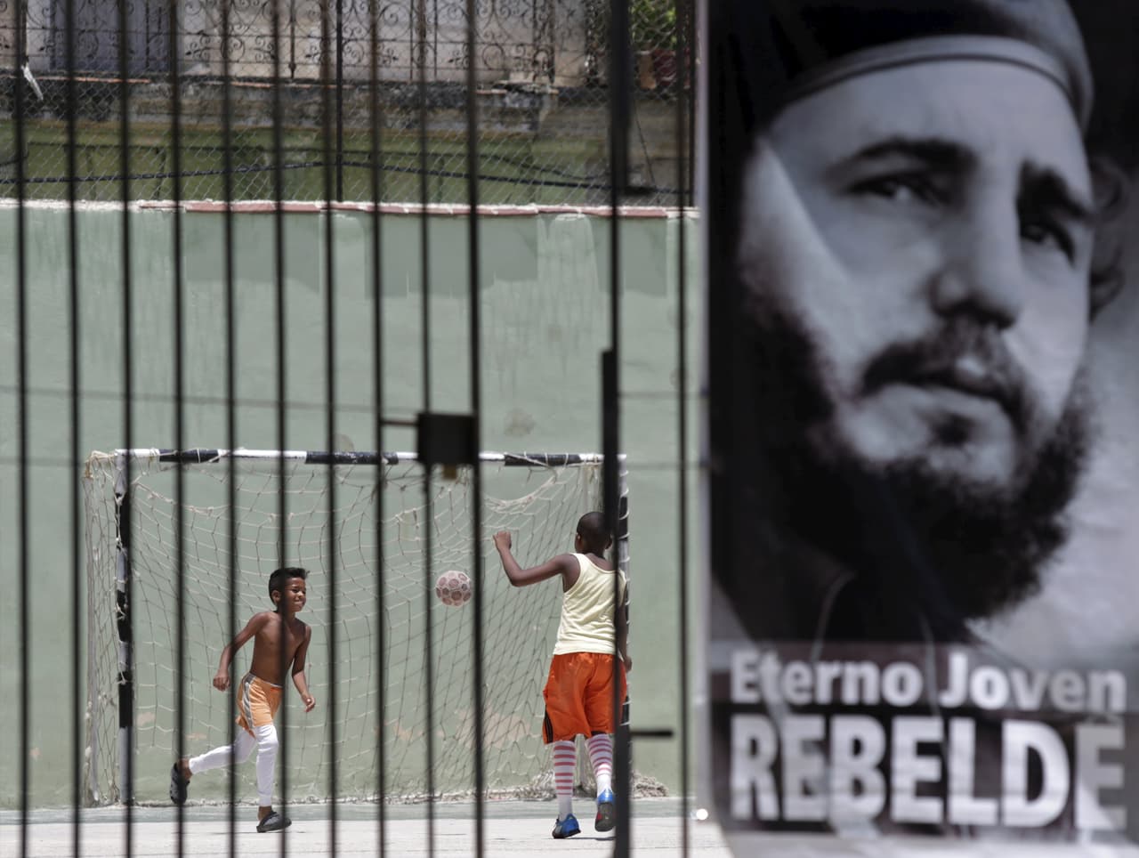 Dos jóvenes jugando al fútbol en un barrio de La Habana detrás de un cartel con la imagen de Fidel Castro.