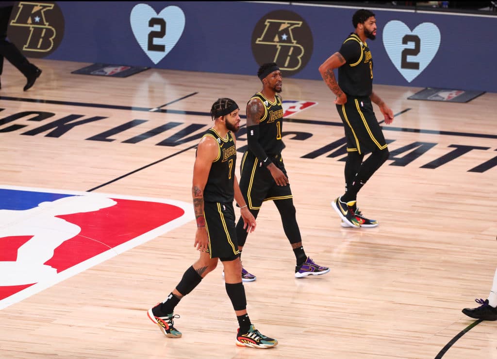 JaVale McGee #7, Kentavious Caldwell-Pope #1, y Anthony Davis #3 de Los Angeles Lakers caminando frente a las pantallas haciendo tributo a Kobe y Gianna Bryant.