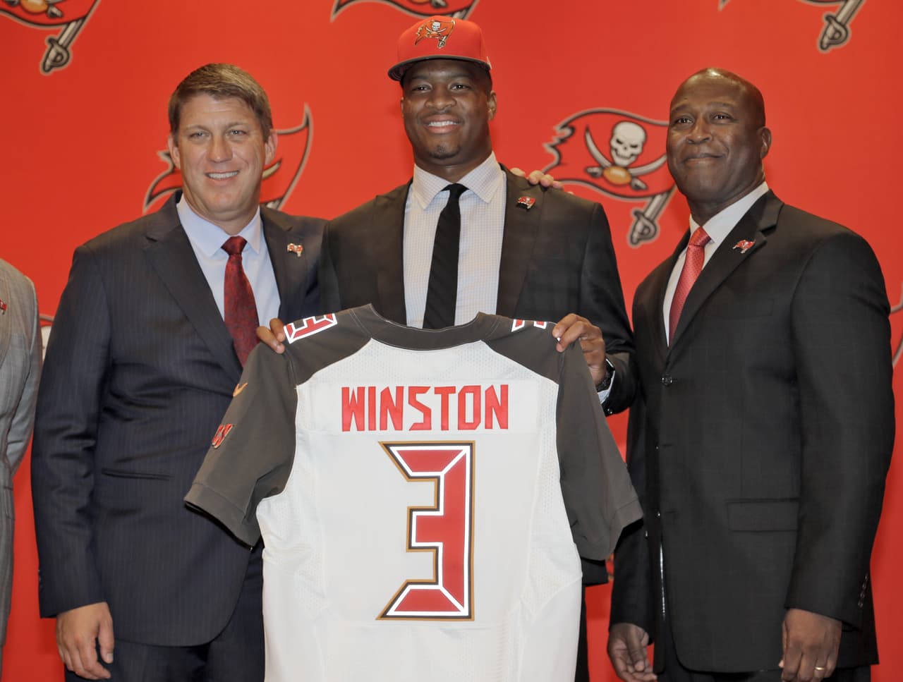 2015 JAMEIS WINSTON | QB Florida State - 
<b>Tampa Bay Buccaneers</b>
<br>
<br>La primera selección global por los Tampa Bay Buccaneers, Jameis Winston (centro) sostiene su jersey con el gerente general Jason Licht, (izquierda) y el entrenador en jefe Lovie Smith (derecha) durante una rueda de prensa el viernes 1 de mayo de 2015, en Tampa, Winston. El ex mariscal de campo de la Florida, fue la primera selección general.