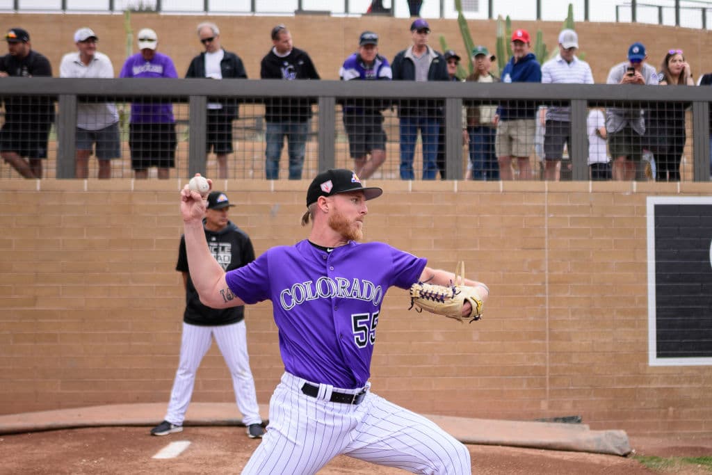 Varios aficionados miran de cerca a Jon Gray de los Colorado Rockies mientras calienta el brazo en el bullpen antes del juego del spring training ante los Oakland Athletics en Scottsdale, Arizona.