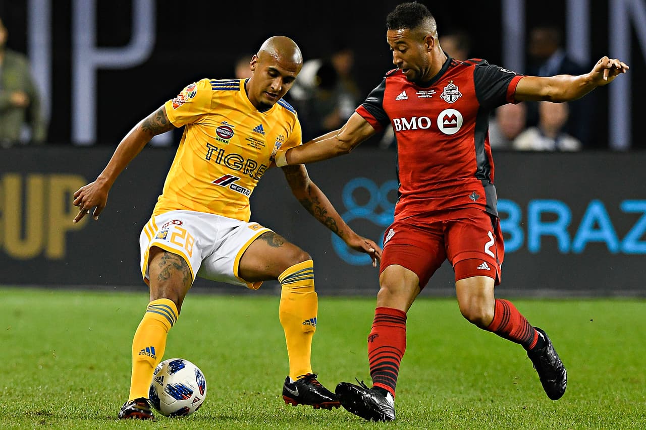 Luis Rodríguez, de los Tigres, y Justin Morrow, de la oncena canadiense, disputando un esférico en el medio del terreno de juego.