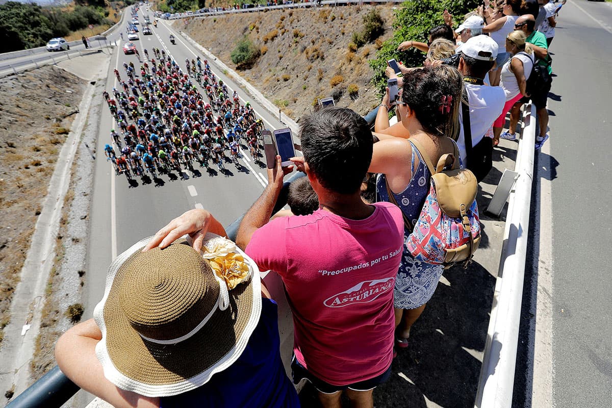 Los fanáticos aprovechan un puente vehícular para tomar fotografías al pelotón de ciclistas.