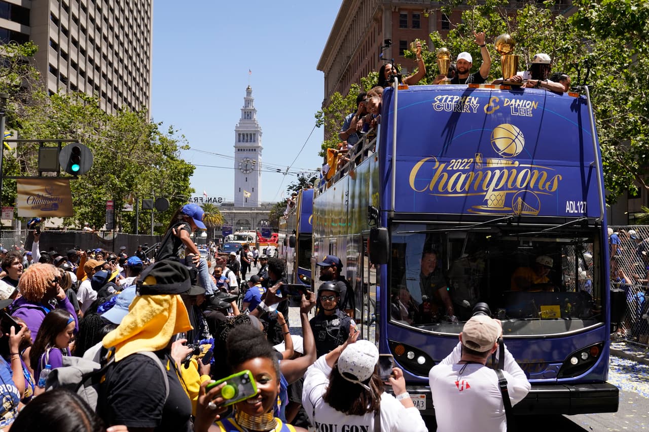 Stephen Curry y Damion Lee, a la derecha, viajan sobre un autobús durante el desfile del campeonato de la NBA Golden State Warriors en San Francisco, el lunes 20 de junio de 2022. (Foto AP/Eric Risberg)