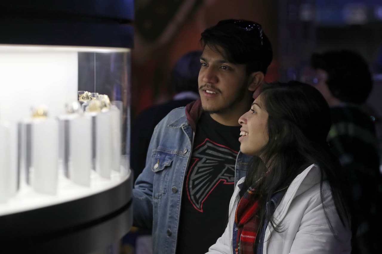 Un par de curiosos aficionados le echan un vistazo a algunos de los anillos que se ciñen quienes tienen el honor de ganar un Super Bowl.