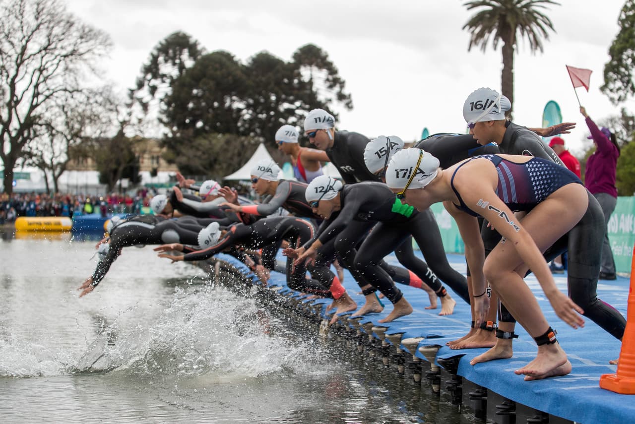 Un grupo de atletas saltan a una piscina dentro de la prueba de natación que forma parte del triatlón mixto por relevos en equipos continentales en un evento que se llevó a cabo en Bosques de Palermo.