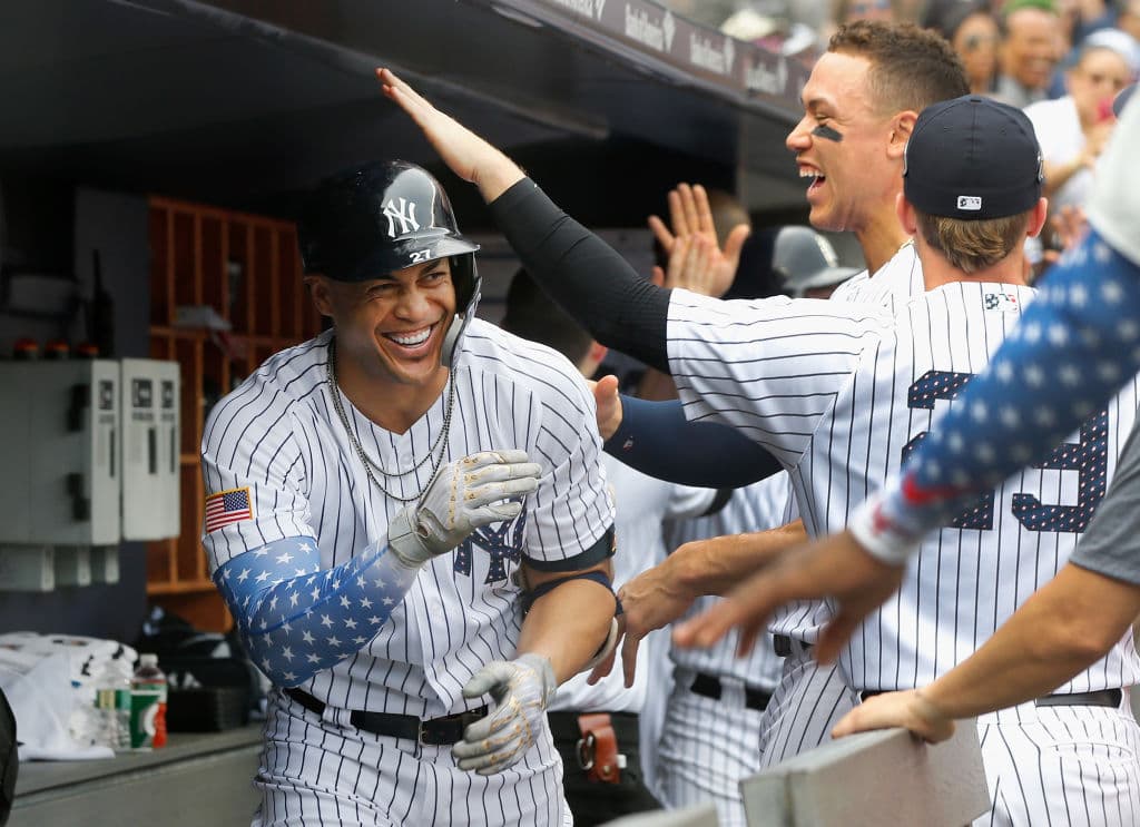 Giancarlo Stanton (izq) de los Yanquis, festeja con sus compañeros en el dugout luego de anotar una carrera ante los Bravos en Yankee Stadium. Las mangas de Stanton con detalles alusivos.