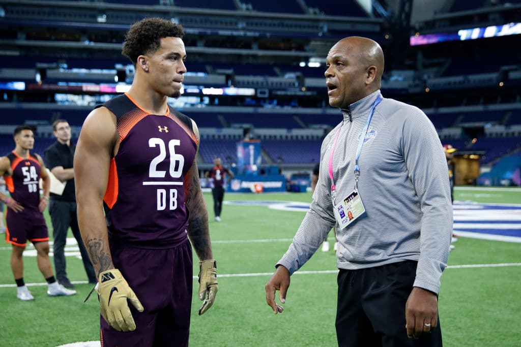 El jugador de perímetro Byron Murphy de la Universidad de Washington conversa con el entrenador de backs defensivos de los Los Angeles Chargers Ron Milus en el quinto día de actividad del NFL Combine en Lucas Oil Stadium, en Indianapolis, Indiana.