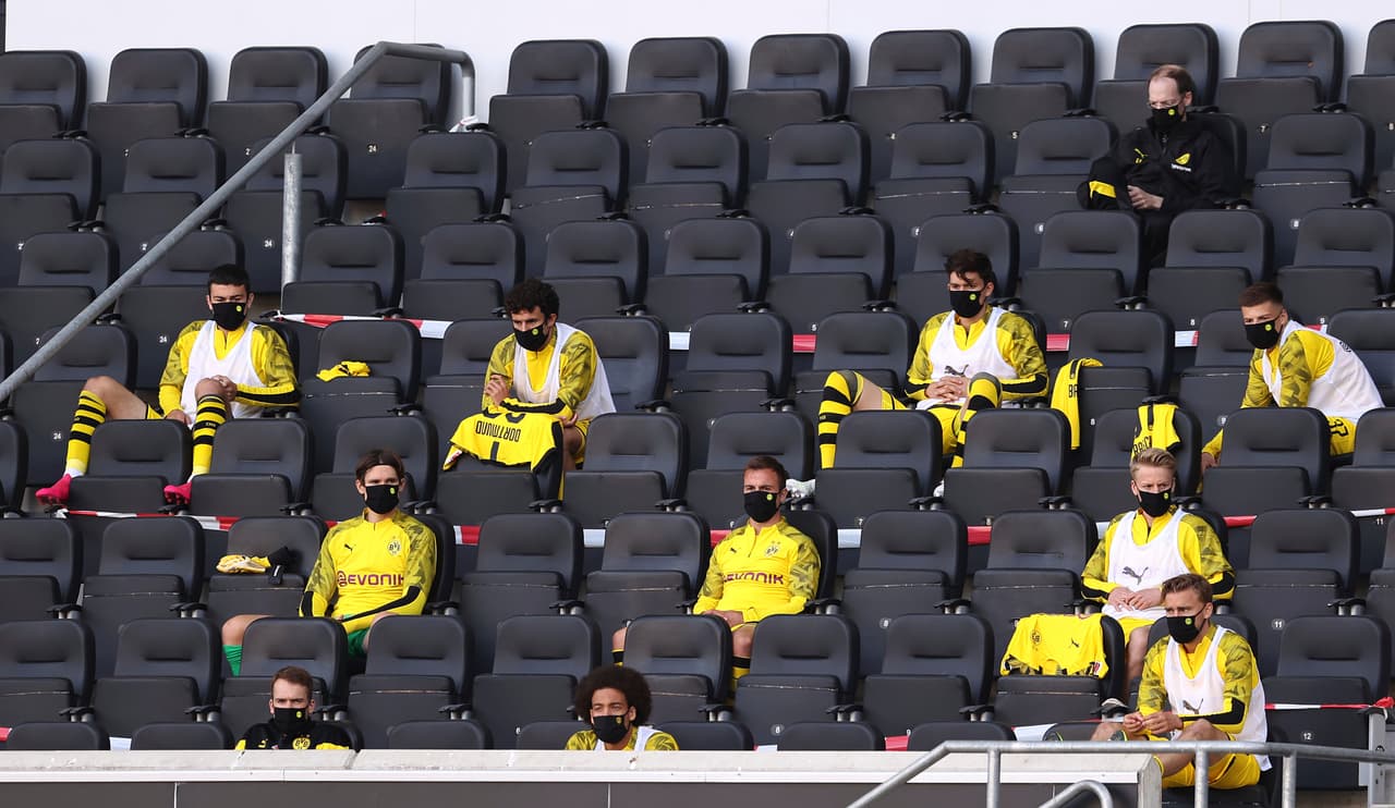 Los jugadores suplentes aprovechan el espacio para sentarse en la tribuna y guardar la distancia social.