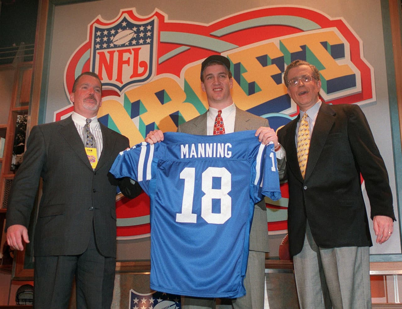 1998 PEYTON MANNING | QB Tennessee - 
<b>Indianapolis Colts</b>
<br>
<br>El quarterback Peyton Manning sostiene el jersey de los Indianapolis Colts mientras está flanqueado por el propietario de los Colts, Jim Irsay (izquierda) y el comisionado de la NFL, Paul Tagliabue, el sábado 18 de abril de 1998 en Nueva York después de ser elegido por los Potros como la selección N° 1 del draft.