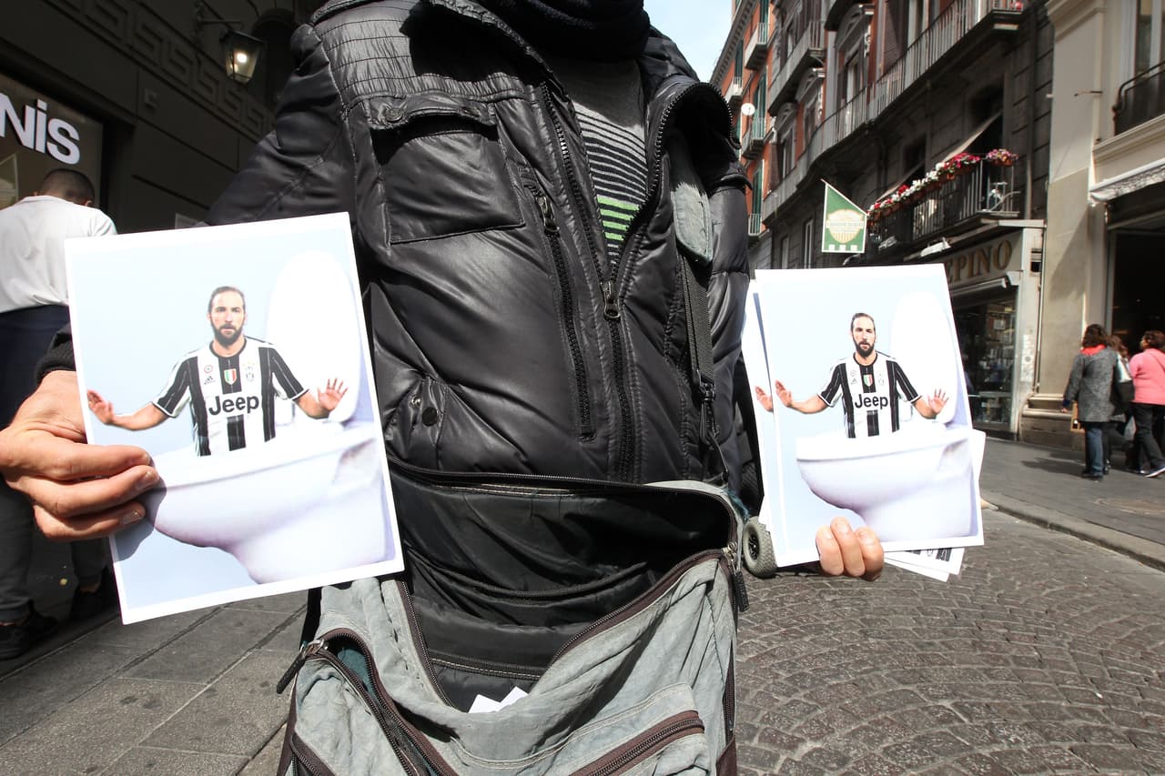 TO GO WITH AFP STORY BY STANISLAS TOUCHOT - A vendor shows posters depicting Juventus' Argentinian forward Gonzalo Higuain in a toilet bowl on March 23, 2017 in a street of Naples. Eight months after leaving team Napoli for Juventus Turin, Gonzalo Higuain prepares a hectic return for the Italian Seria A football match Napoli vs Juventus at San Paolo stadium, where the rancor against the Argentine "traitor" remains immense. / AFP PHOTO / CARLO HERMANN (Photo credit should read CARLO HERMANN/AFP/Getty Images)