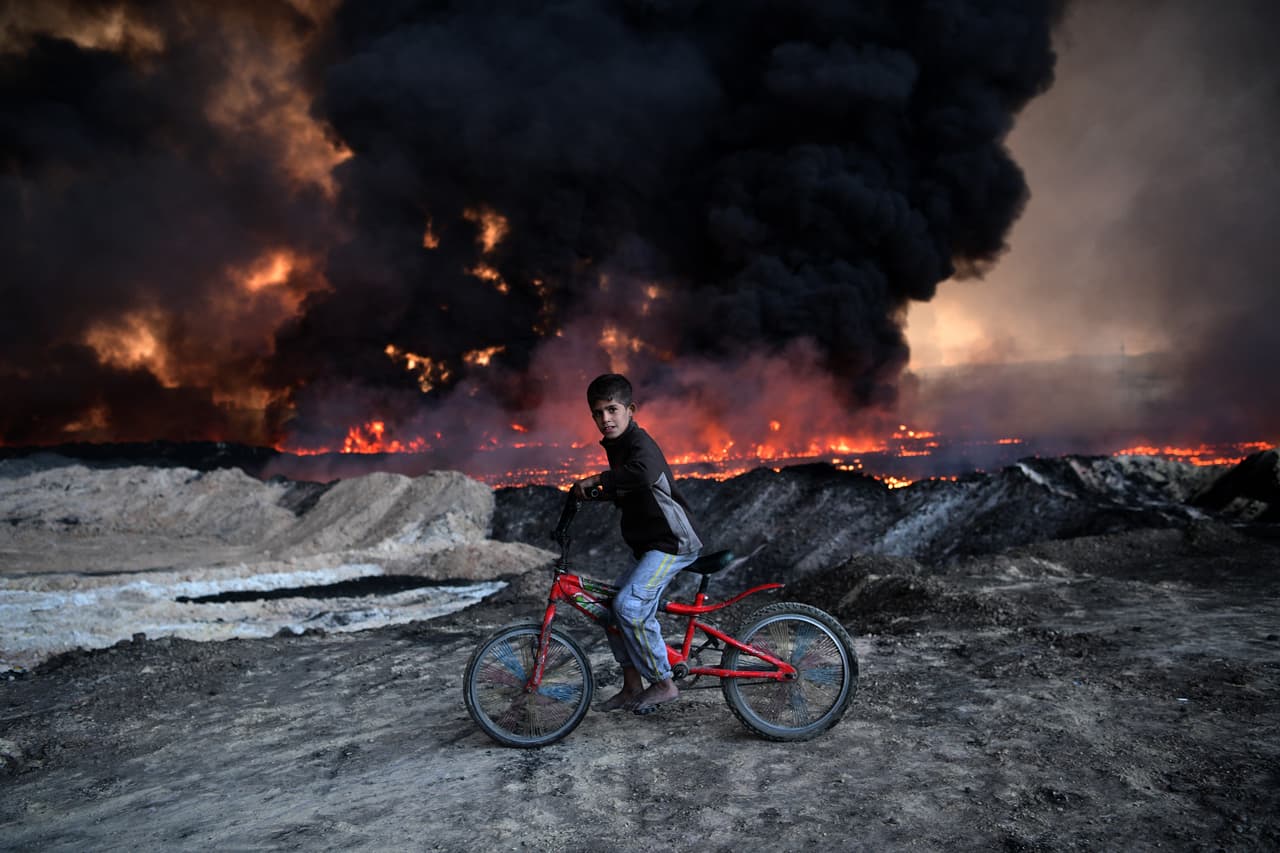 <b>El ciclista de Mosul.</b> Un joven iraquí se desplaza en bicicleta frente a un campo de petróleo que fue incendiado por los combatientes de ISIS en Mosul, Irak. 21 de octubre de 2016.