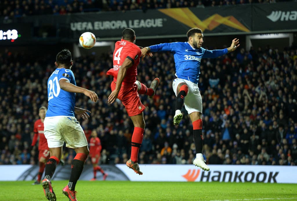 Connor Goldson trata de rematar a puerta, pero el defensa Jonathan Tah le gana el balón y aleja el peligro de su arco.
