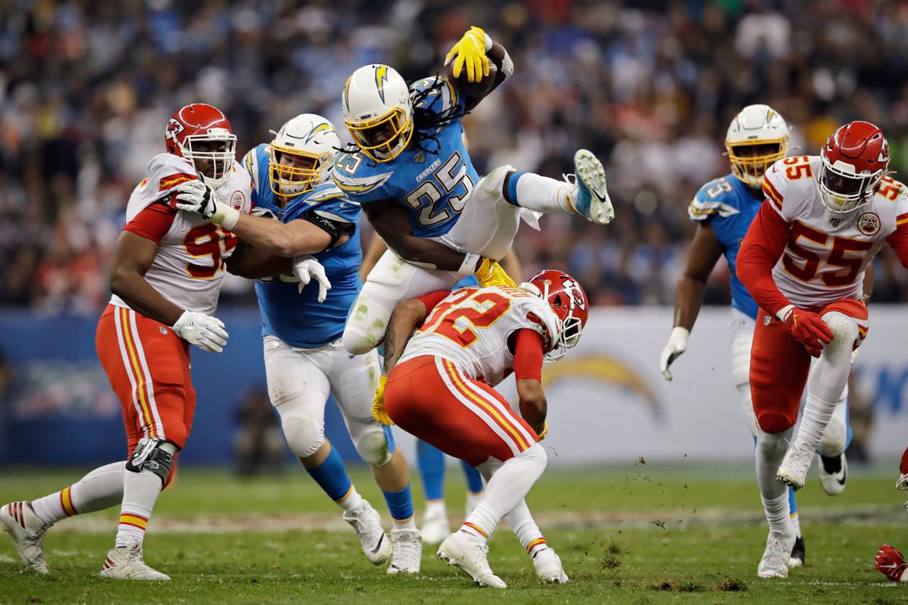 ¡Enorme! Melvin Gordon brinca sobre Tyrann Mathieu, de los Chiefs, que intentaba derribarlo para frenar su avance.