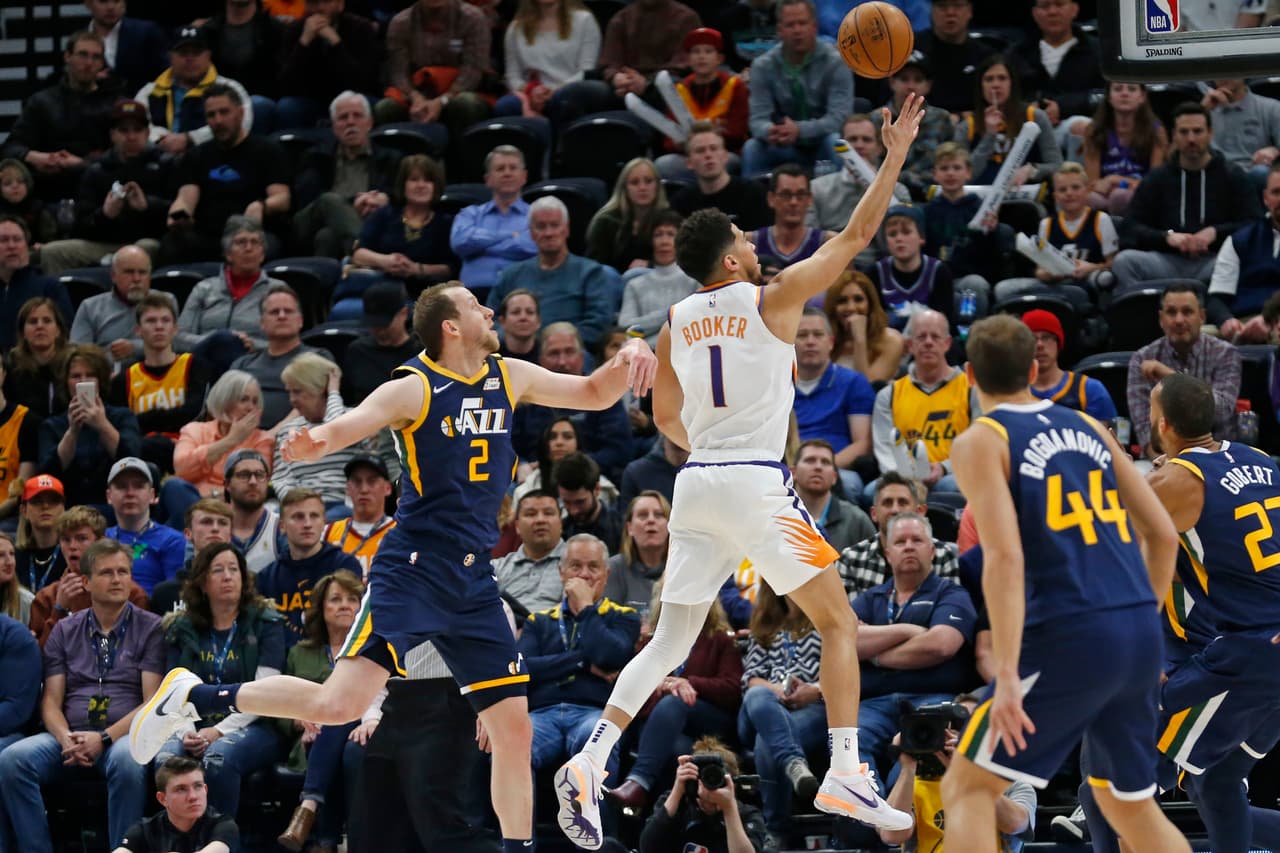 El guardia de los Phoenix Suns Devin Booker consigue dos puntos para los Suns, que terminarán ganando el encuentro; Joe Ingles lo persigue pero no logra evitar que el rival enceste.