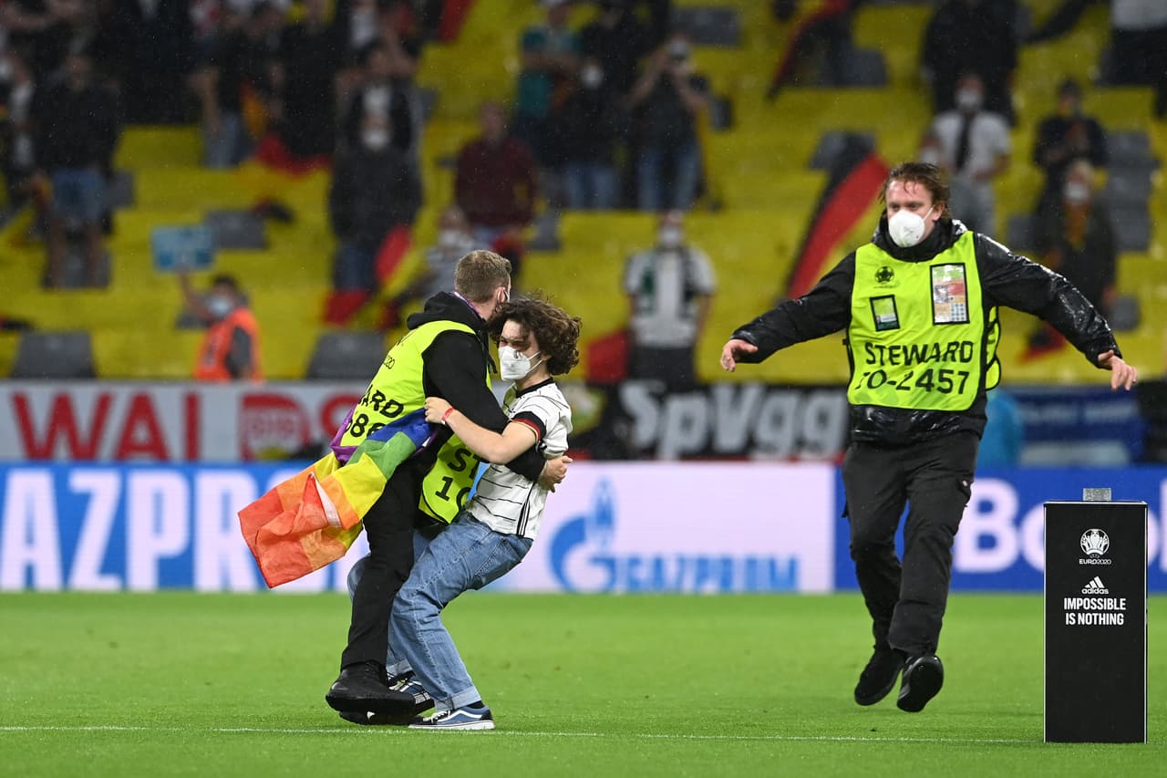 MUNICH, GERMANY - JUNE 23: A pitch invader with a rainbow flag is seen being removed from the pitch by stewards prior to the UEFA Euro 2020 Championship Group F match between Germany and Hungary at Allianz Arena on June 23, 2021 in Munich, Germany. (Photo by Christof Stache - Pool/Getty Images)