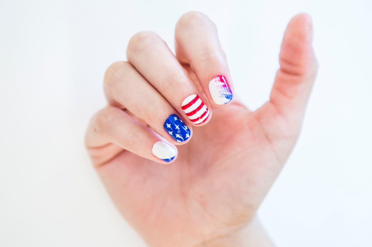 Estados Unidos: Da 2 capas de azul en la uña del dedo anular y 2 más de blanco en el resto de las uñas. En el dedo meñique pinta con un pincel un triángulo en la parte inferior de la uña. Para las estrellas dibuja cruces pequeñas con un pincel muy delgado y con ayuda de un pincel más grueso traza líneas horizontales de orilla en la del dedo medio. Moja la mitad de un pincel mini abanico de rojo y la otra de azul, barre de un lado al centro.