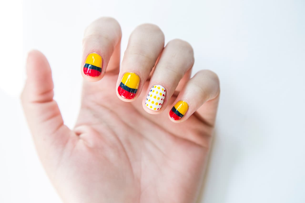 Colombia: Da 2 capas de esmalte blanco en el dedo anular y 2 capas en tono amarillo en el resto de las uñas, deja secar. En la uña del dedo meñique, medio y anular traza una línea horizontal en azul y otra más gruesa en rojo. Ayúdate con un puntero para hacer los puntos en amarillo, azul y rojo en la uña del dedo anular.