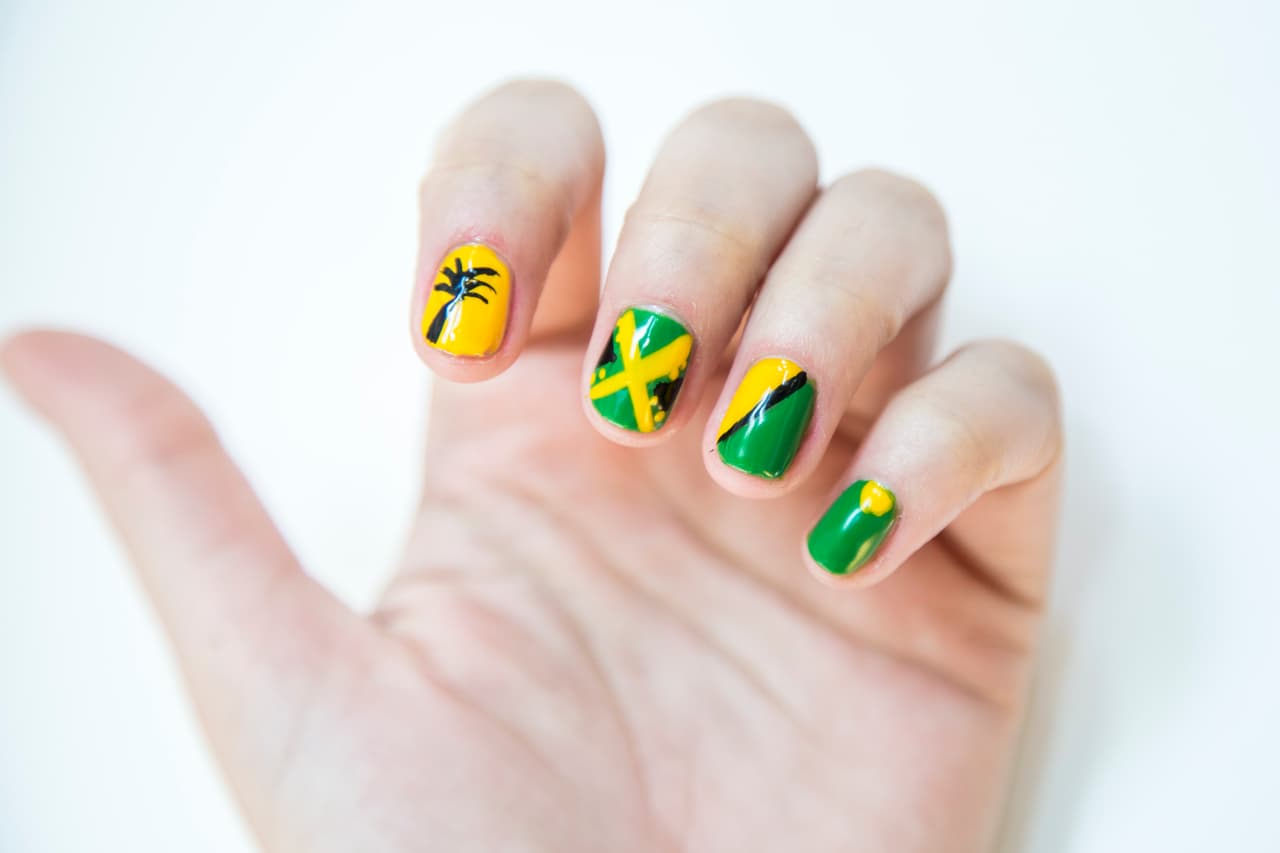 Jamaica: Aplica 2 capas de verde en las uñas del meñique, medio y la mitad del anular. Da 2 capas de amarillo en la uña del índice, y dibuja un triángulo en la lúnula del meñique y rellena la otra mitad del anular. Con un pincel delgado traza una línea diagonal negra entre los 2 colores. Con amarillo traza una X en la uña del medio y decora con puntos. Traza 2 triángulos negros a los costados. Con un palillo dibuja una palmera en el índice.