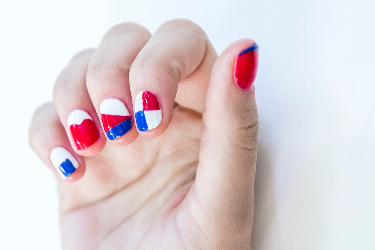Panamá: Da 2 capas de blanco en la uña del meñique y 2 de rojo en la del pulgar. En el meñique dibuja con un pincel un cuadrado azul y en el pulgar la línea del francés. En la uña del dedo anular forma 2 semicírculos con el rojo. Rellena con un pincel liner el resto con blanco. En el dedo medio haz triángulos con los 3 colores y en el índice dibuja con esmalte blanco una cruz en el centro de la uña y rellena cada cuadro alternando los 3 tonos.