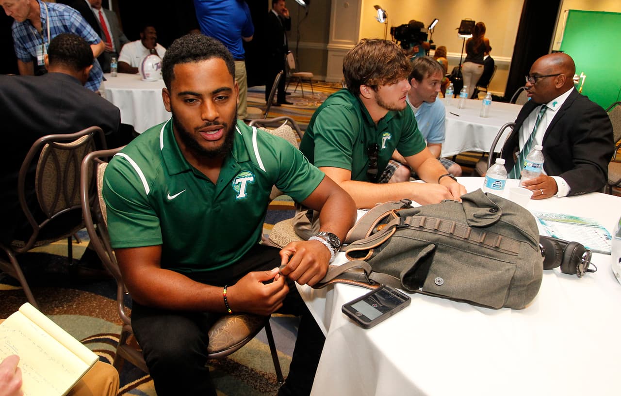 Tulane linebacker Nico Marley, left, speaks with a reporter as teammate Tanner Lee, center, and head coach Curtis Johnson, right, are also interviewed at the American Athletic Conference NCAA college football media days in Newport, R.I., Tuesday, Aug. 4, 2015. (AP Photo/Stew Milne)