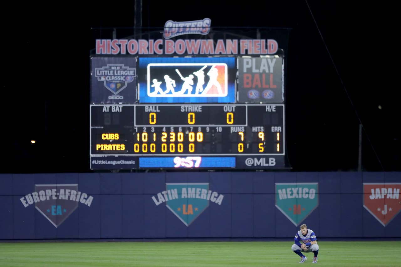 Ian Happ de los Chicago Cubs en los jardines, mientras aparece de fondo la peculiar pizarra del Bowman Field en el Little League Classic en Williamsport, Pennsylvania.