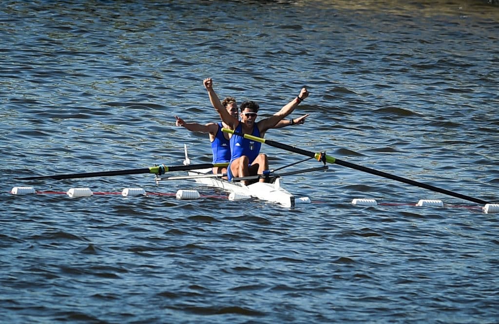 Dos remeros italianos levantan los brazos en su embarcación mientras cruzan la línea de llegada con buenos resultados. Un deporte añejo y siempre atractivo, el remo.