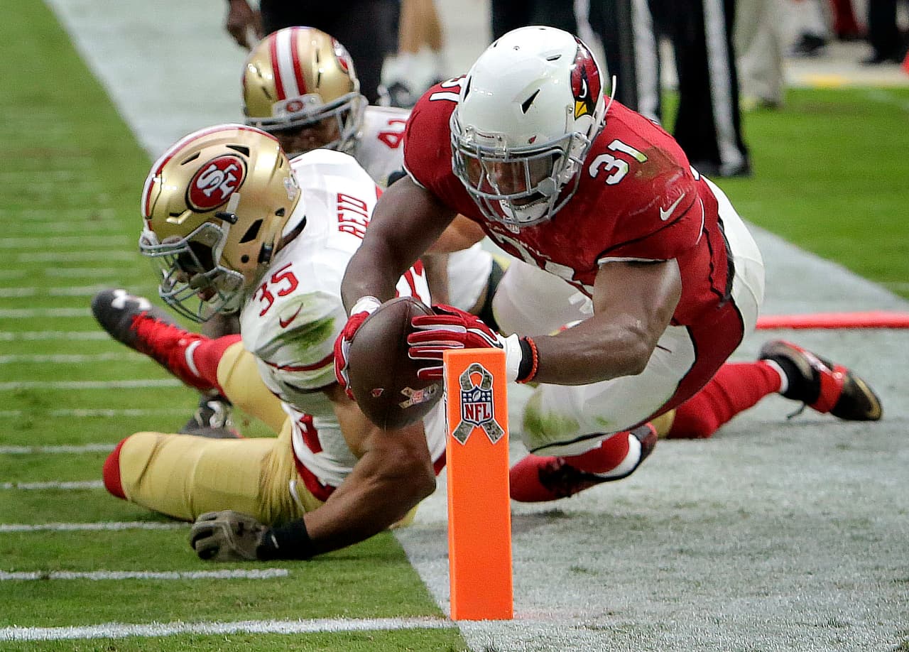 El esfuerzo del corredor de Arizona, David Johnson, por alcanzar las diagonales psando por el safety Eric Reid de San Francisco.