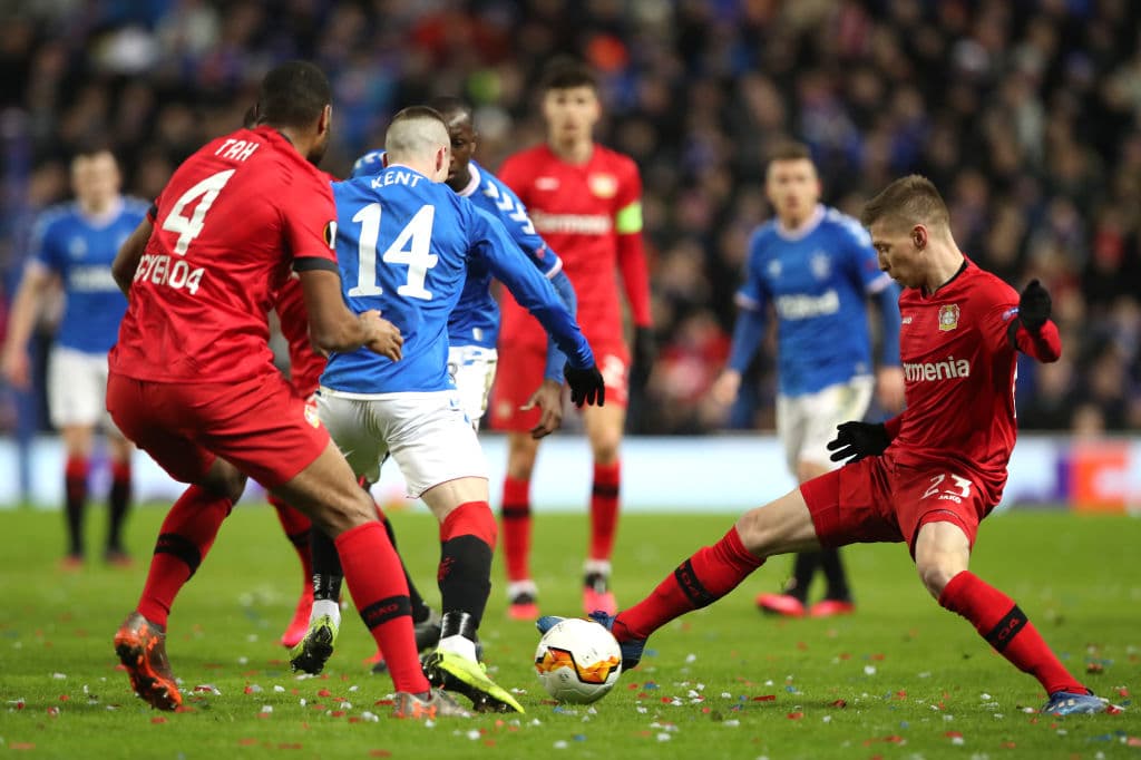 Ryan Kent of Rangers logra safarse de la presión de dos jugadores y se apoya con su compañero Steven Davies.