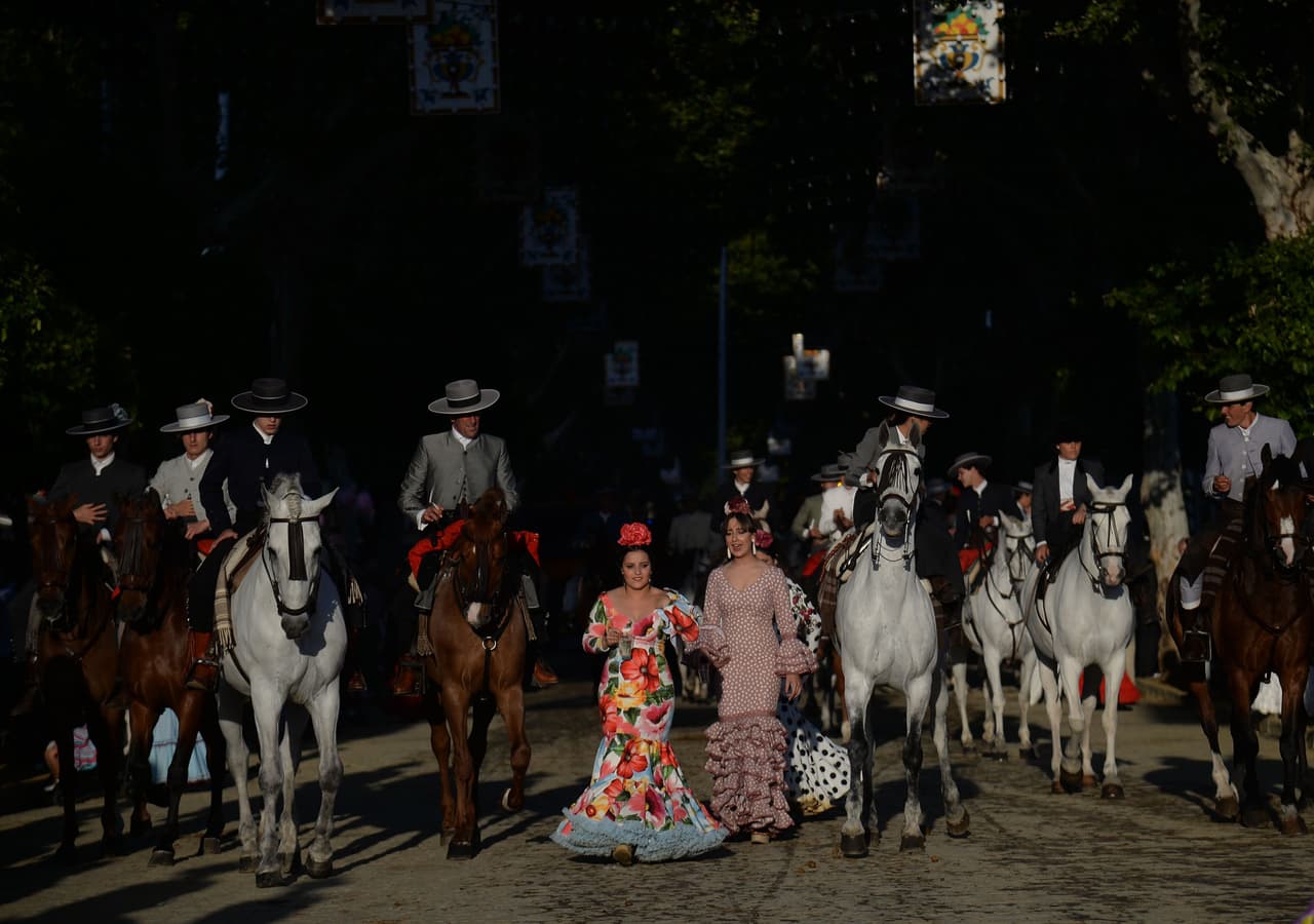 Las personas con trajes tradicionales sevillanos montan a caballo y caminan por las calles de la ciudad durante la "Feria de Abril".
<br>