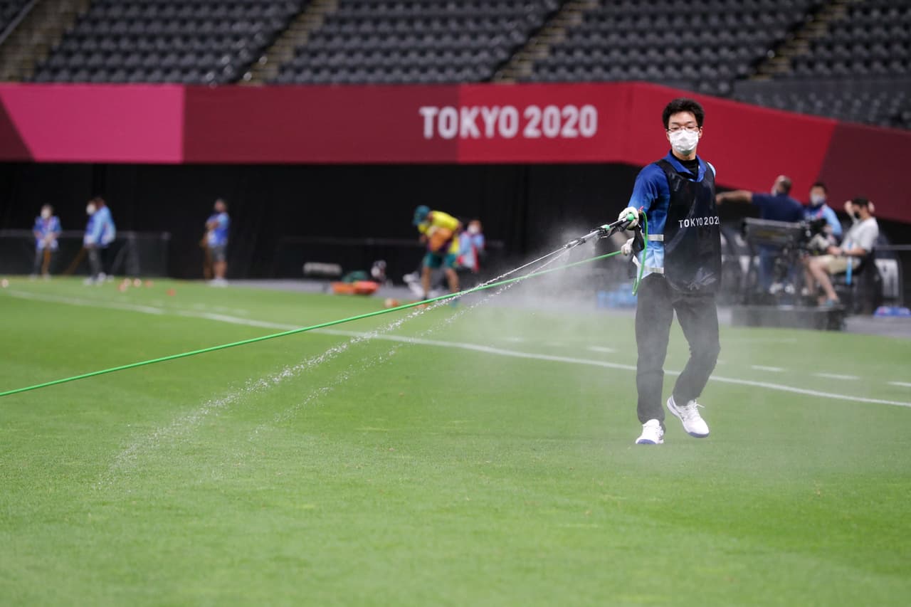 Un empleado rocía desinfectante contra el coronavirus sobre el césped del estadio donde se está jugando la primera ronda del torneo olímpico de futbol. 22 de julio.
