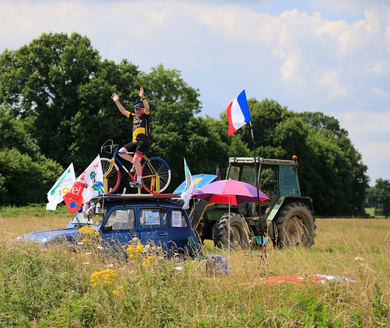 Año con año el ciclismo demuestra ser una pasión por dondequiera que pasa el Tour en Francia. Aquí vemos a un aficionado montado en una bicicleta, pero en el techo de un automóvil.