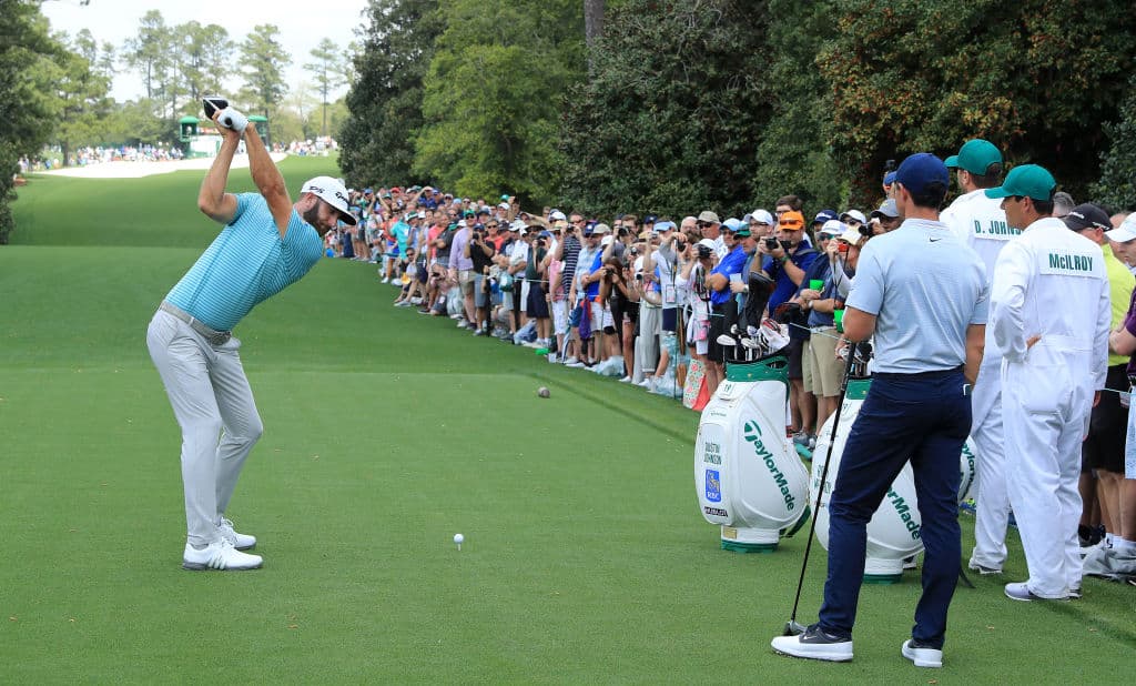 Mientras Dustin Johnson se dispone a hacer su tiro de salida, una multitud lo observa, prueba del gran interés que reviste este torneo entre los apasionados al golf.