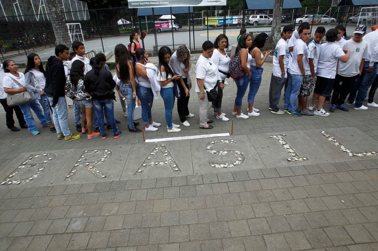 Aficionados colombianos esperan en fila a entrar en el estadio para participar en el homenaje, al lado de un conjunto de velas que forman la palabra Brasil.